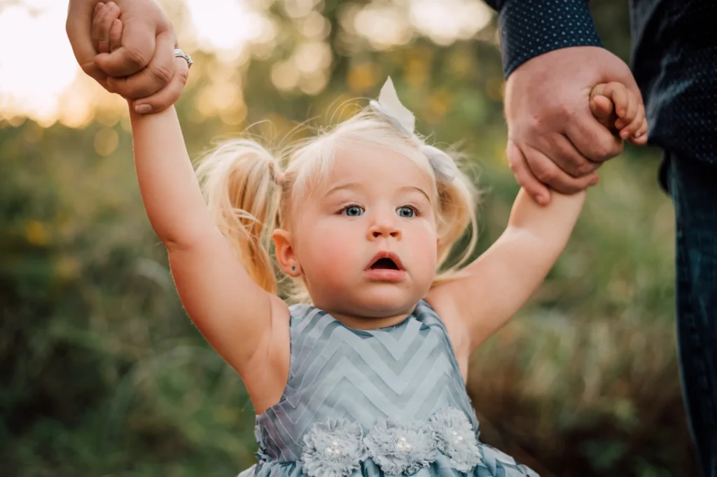A young girl being held by her parents.