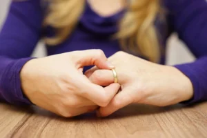 Women wearing a blue shirt, taking off a gold wedding ring.