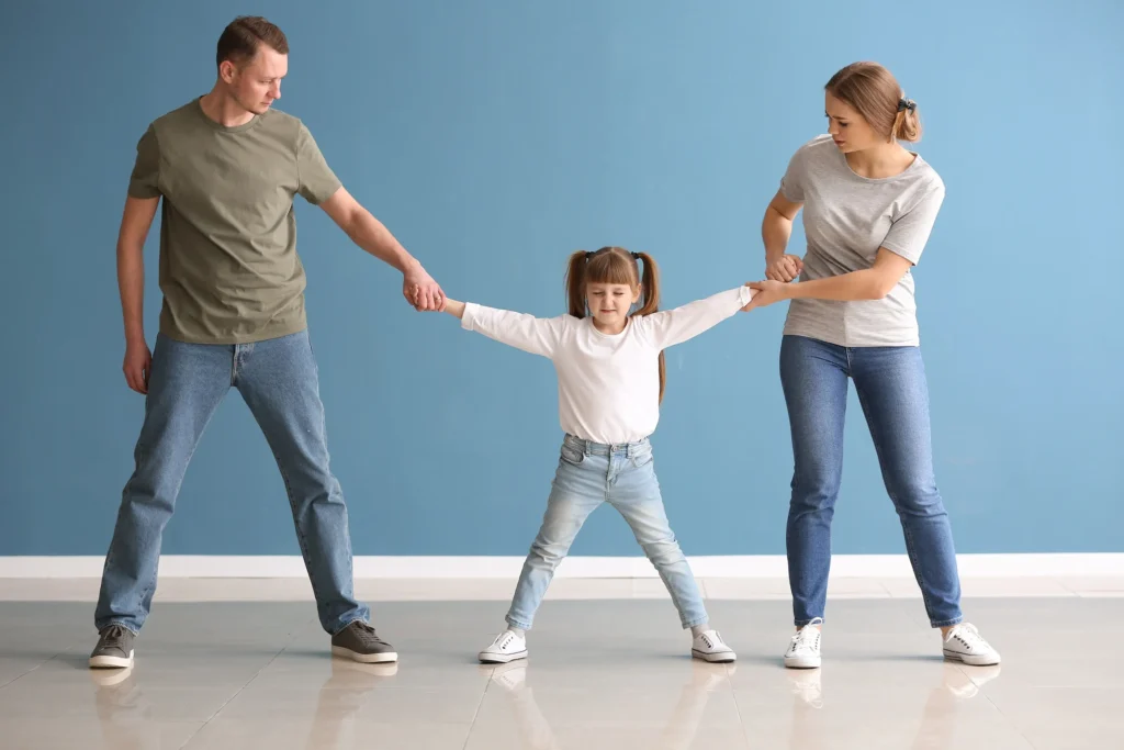 A mom and dad pulling on a child standing between them.