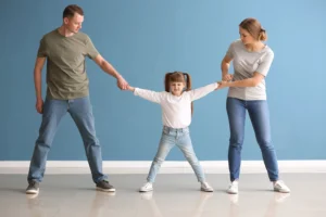 A mom and dad pulling on a child standing between them.