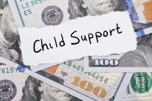 Several one-hundred dollar bills scattered and a note that reads Child Support.