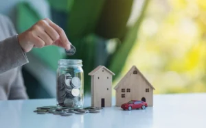 Two wood model homes and a jar of coins on a table.