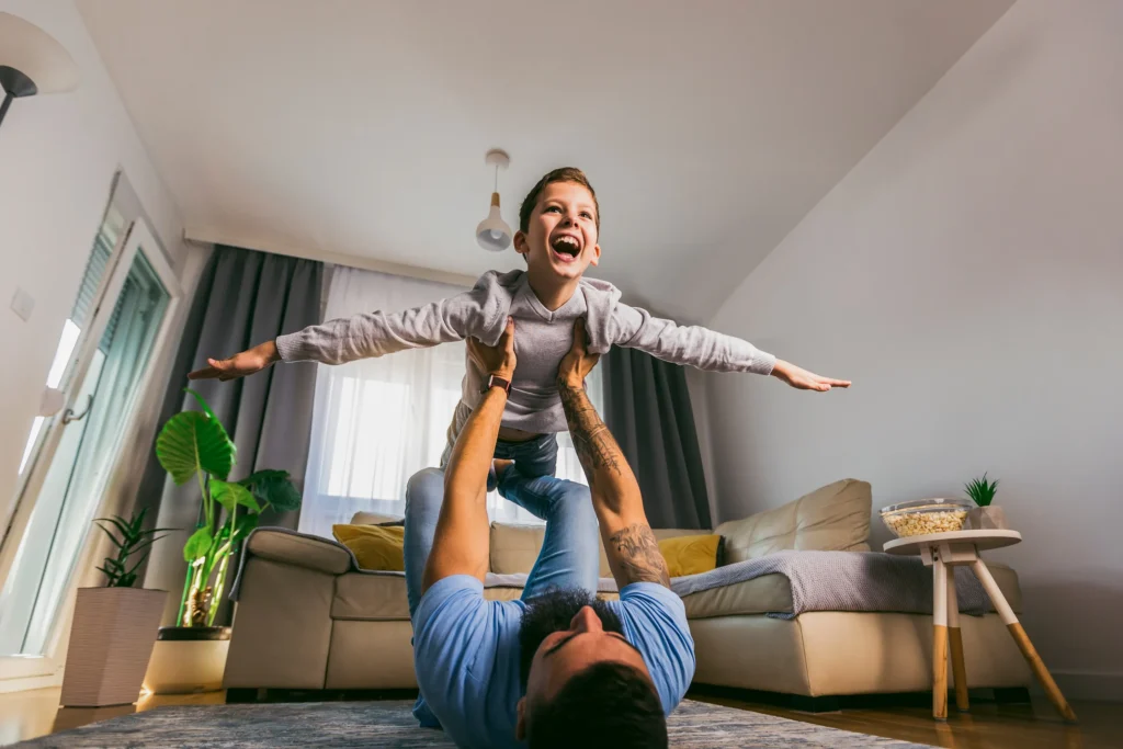 A father holding up his son with his arms out like an airplane.