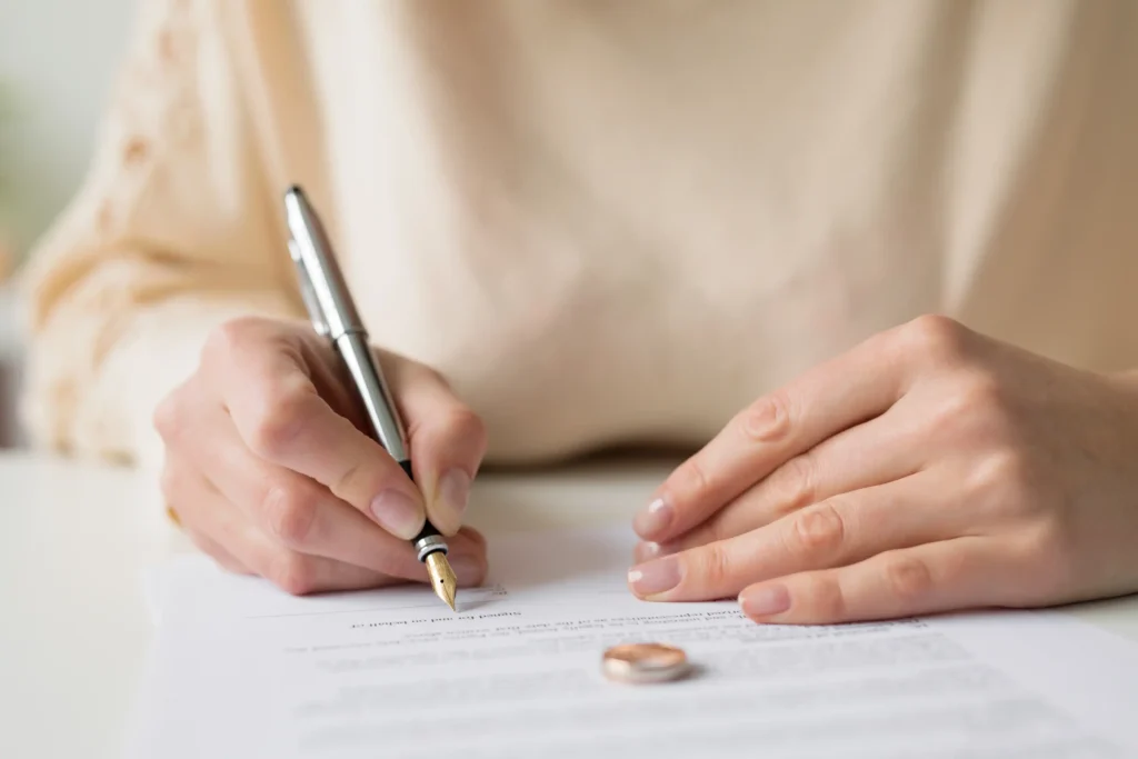 A woman signing papers with her wedding ring on the paper.