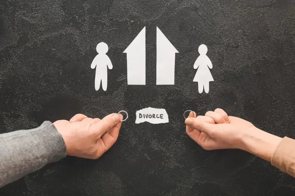 A ripped paper home with divorce written at the bottom with two people holding their wedding rings.