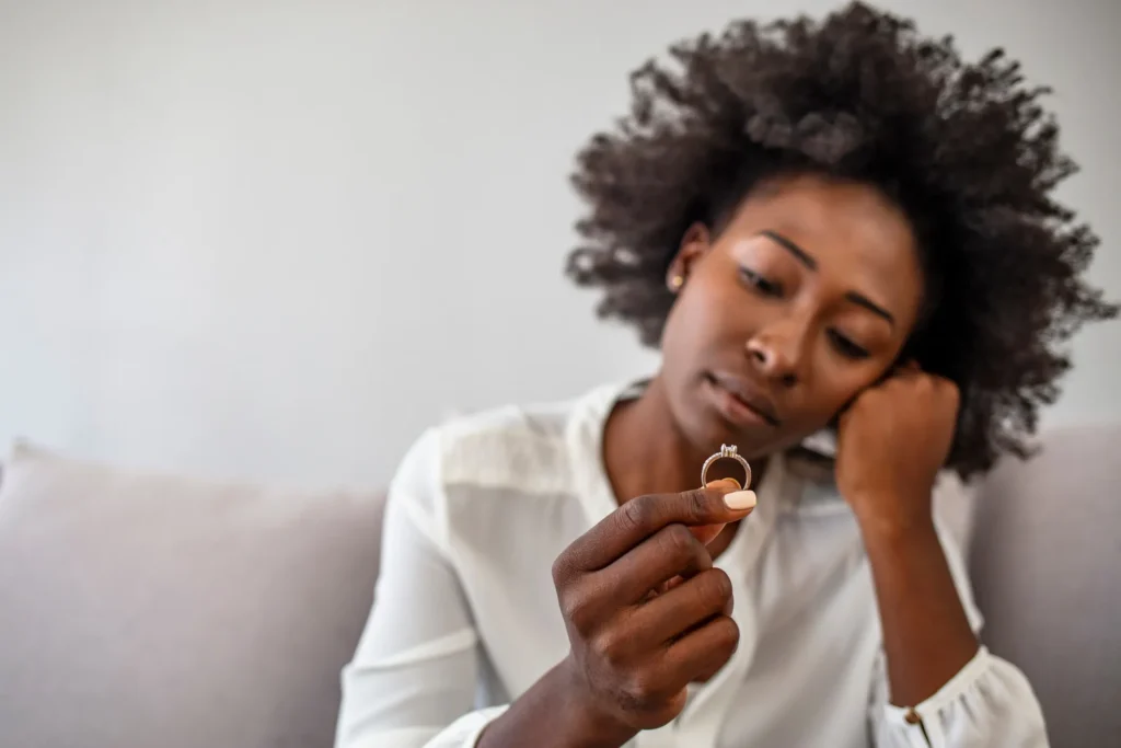 A woman resting her head on her hand looking at her gold wedding ring.